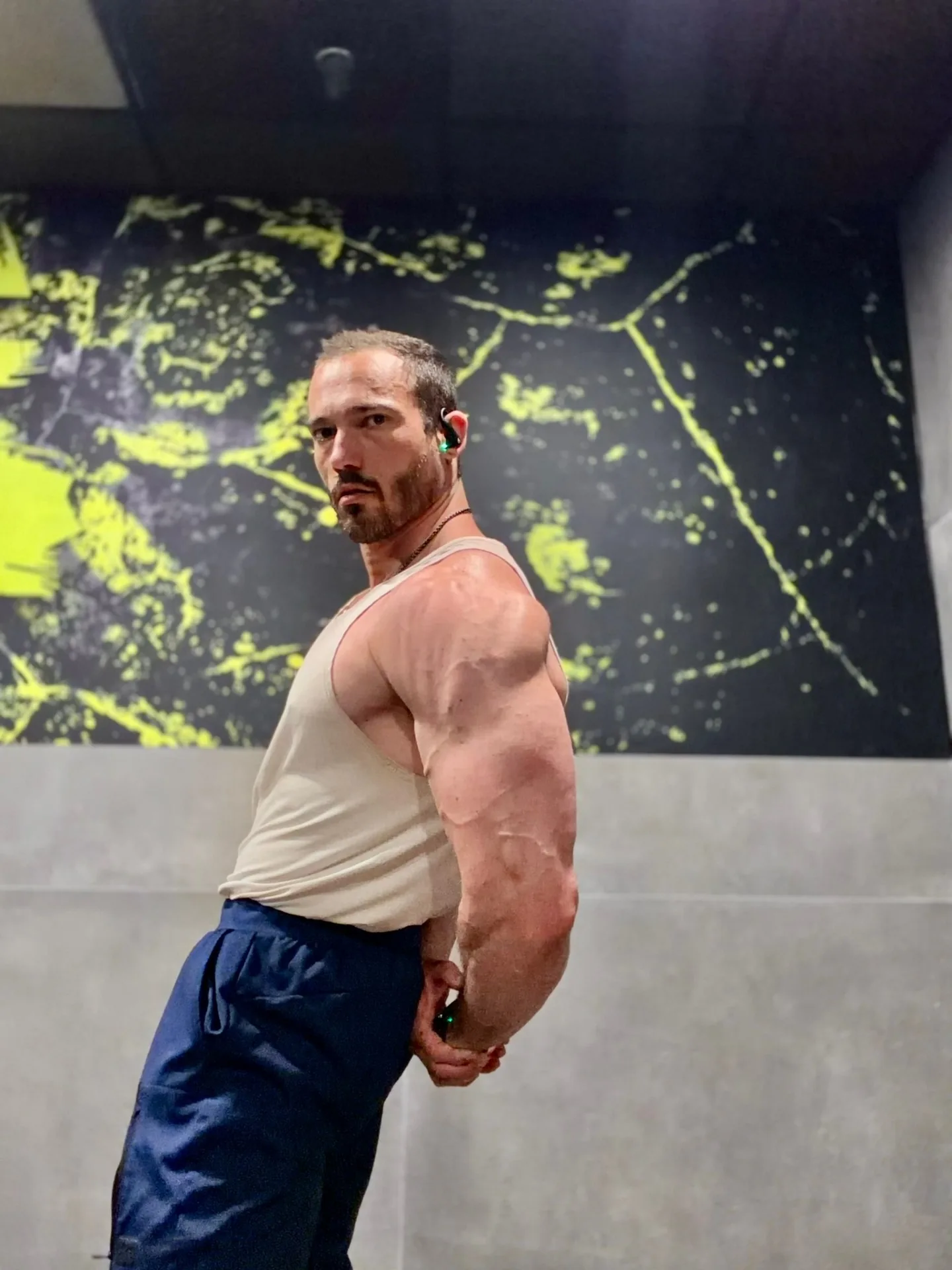The Anabolic Architect coach in a moody industrial gym, holding a side-tricep pose with high-contrast lighting