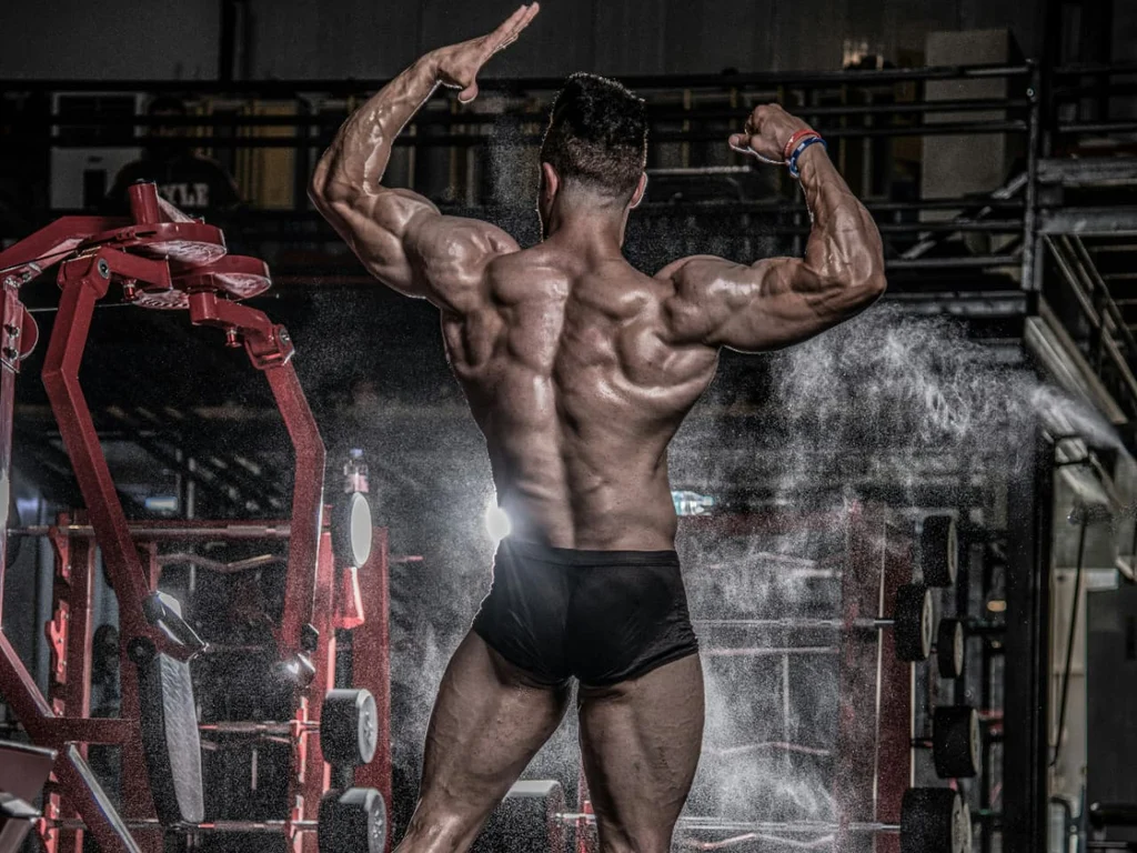 Competitive bodybuilder holding a rear double biceps pose under dramatic gym lighting